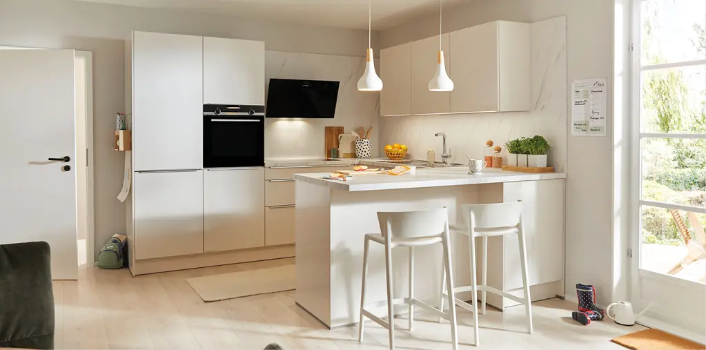 Helle moderne Küche in Weiß mit Kochinsel, Barhockern und integrierten Elektrogeräten. Klare Linien, viel Tageslicht und hochwertige Materialien zeigen zeitloses Küchendesign für offene Wohnkonzepte.